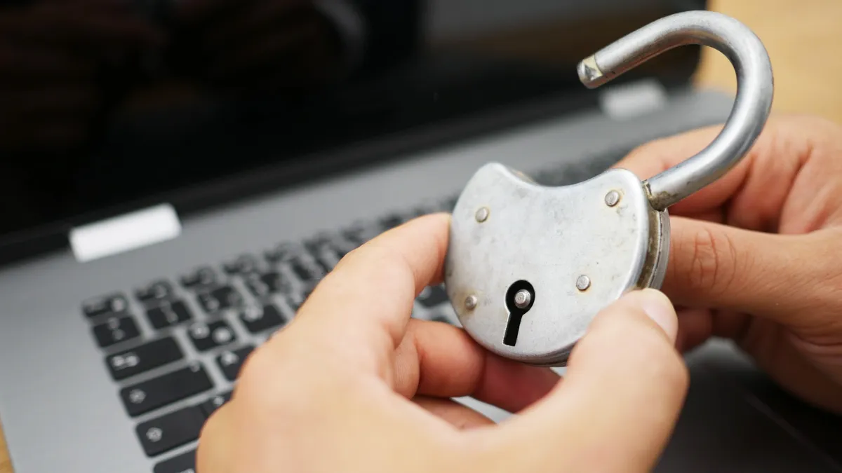 Imagem de mão segurando um cadeado em frente à um notebook